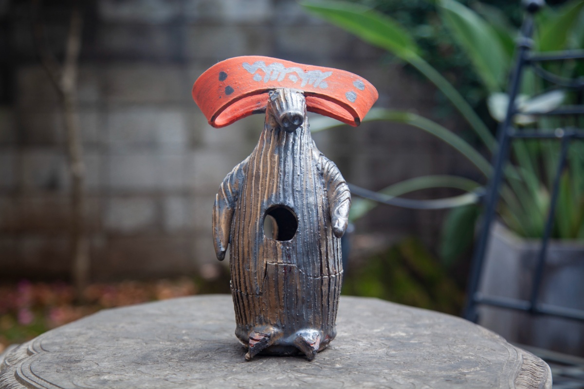 稲垣美穂氏による手作り野鳥巣箱。庭園の石製台の上に展示された、縦方向の木目彫刻が施された茶色い木製本体に、赤い屋根が付き、テントウムシをモチーフとした黒い斑点が描かれている