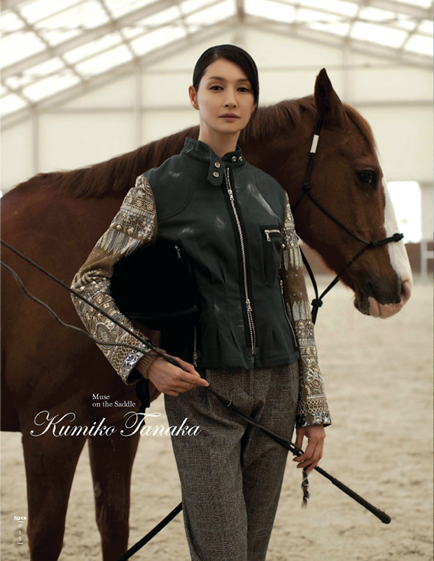 温室の中で栗毛の馬の横に立つ日本人女性。黒いレザーベストと白とグレーのツイード柄ジャケットを着用し、馬の手綱を握っている。テキストに「Muse on the Saddle Kumiko Tanaka」と記載されている