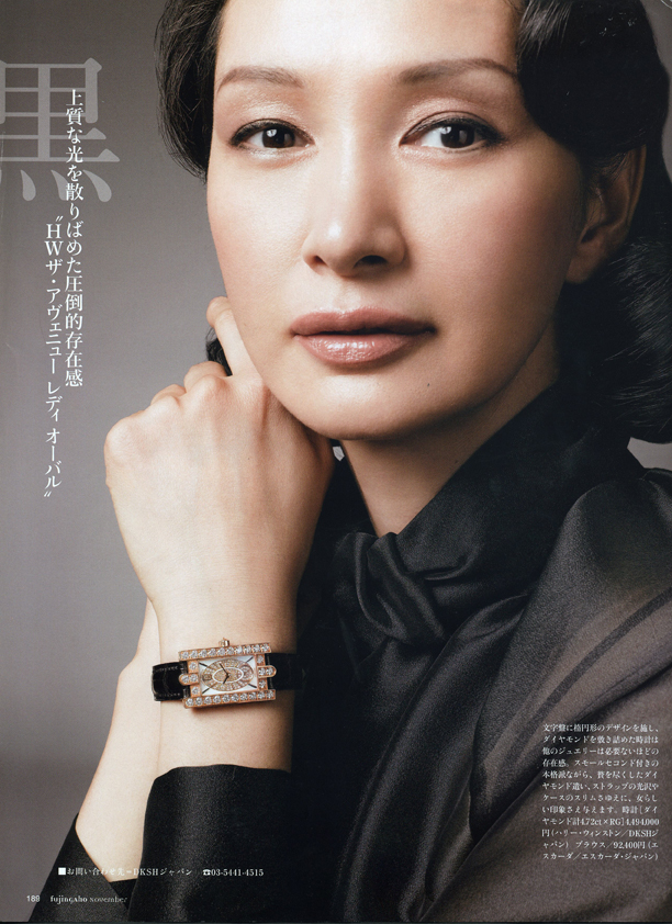 グレーの背景で、黒いシャツを着た日本人女性の顔アップ。手首に装飾的なゴールドとブラックの高級腕時計を着用し、チンに手を添えている。左側に日本語のテキストが記載されたファッション雑誌のページ